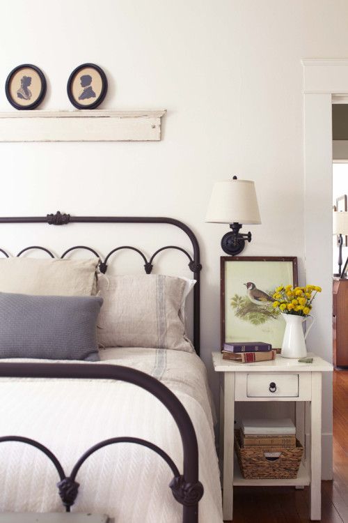 a simple farmhouse bedroom with vintage furniture, a metal bed and a nigthstand with a basket