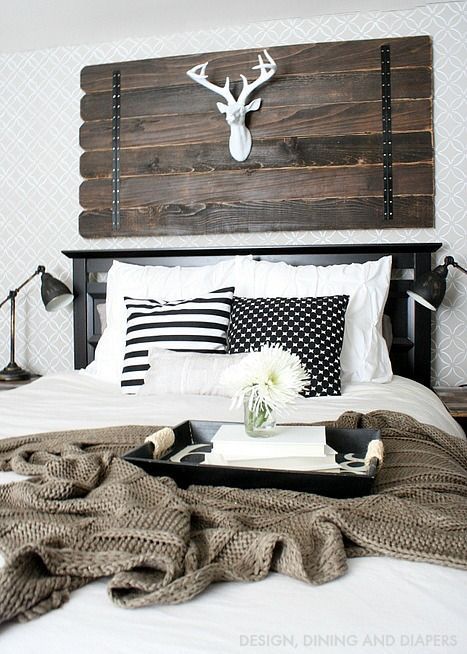 a farmhouse bedroom with a weathered wood art with a fake deer head, a black bed, vintage metal lamps