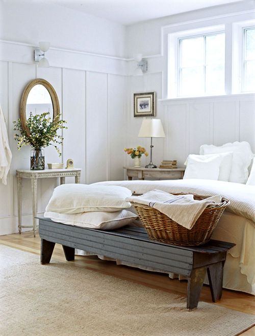 a neutral farmhouse bedroom with weathered wood nightstands, a refined vanity, a dark bench and a basket