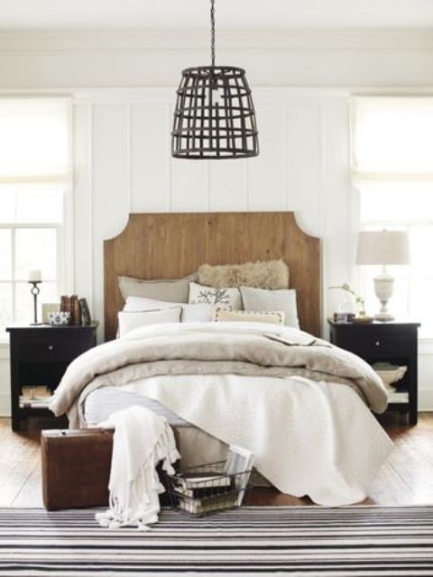 a chic farmhouse bedroom in neutrals is spruced up with black nightstands, a wooden bed, a metal lampshade
