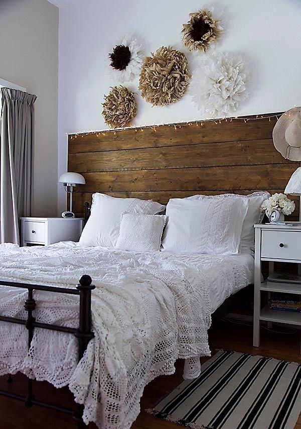 a welcoming farmhouse bedroom with a large wooden headboard, simple white nightstands, paper flowers over the bed for decor