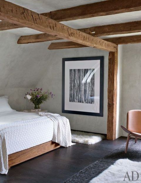 a farmhouse meets vintage bedroom with many wooden beams, a dark stained floor and white plaster walls