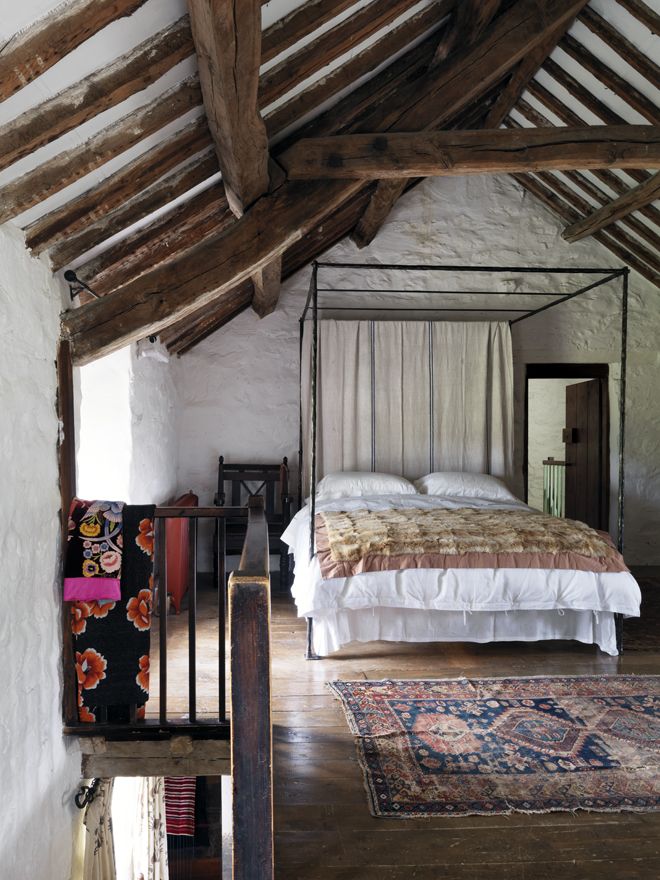 an attic farmhouse bedroom with stone walls and wooden beams, a large metal bed and boho rugs
