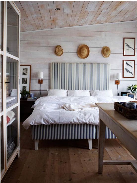 a farmhouse bedroom with whitewashed wood, a striped upholstered bed and straw hats for decor