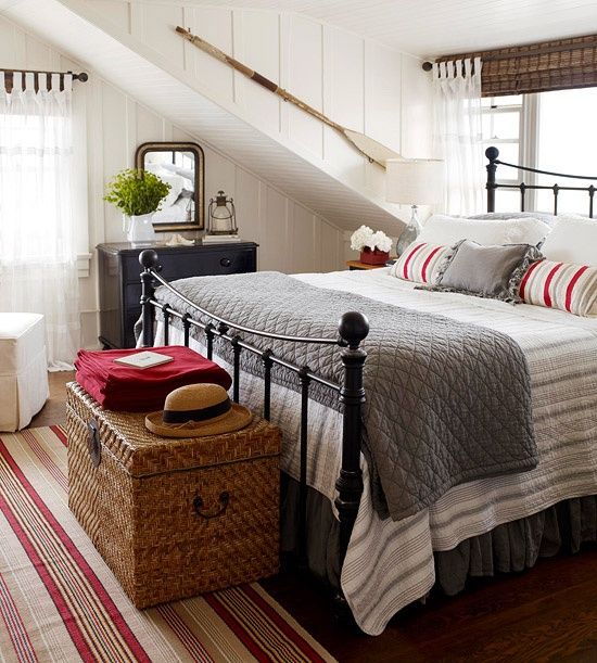 a farmhouse meets beach bedroom with white wooden panels, a wicker chest, a forged bed and beachy touches