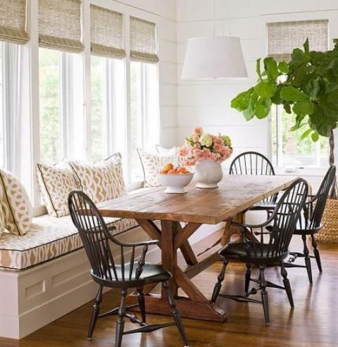 a modern farmhouse dining nook with a windowsill upholstered bench, a wooden table and dark chairs plus wicker shades