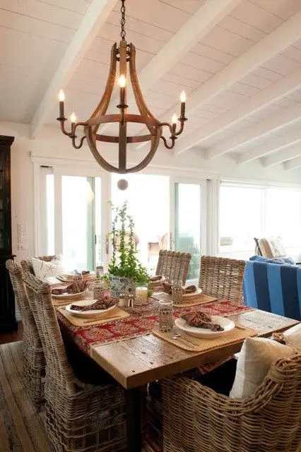a farmhouse dining space with a wooden table and wicker chairs, a wooden chandelier and greenery