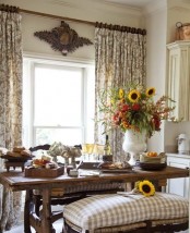 a traditional farmhouse dining space with neutral printed textiles, rich-stained wood, rattan benches and bright florals