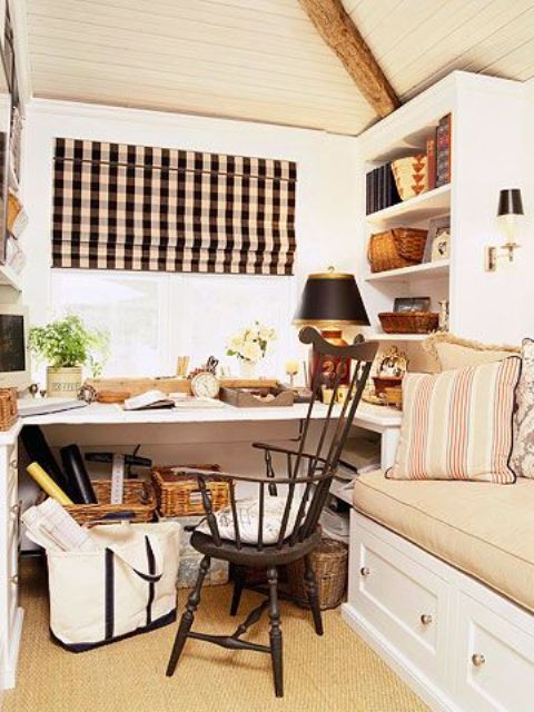 A neutral and cozy farmhouse home office with a built in desk, bookshelves and a daybed, a vintage chair, a black lamp and a plaid curtain