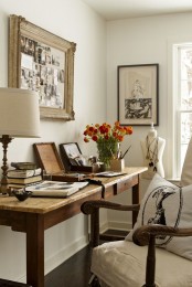 a vintage farmhouse home office with a wooden desk, a refined chair, chic artworks and a table lamp and blooms