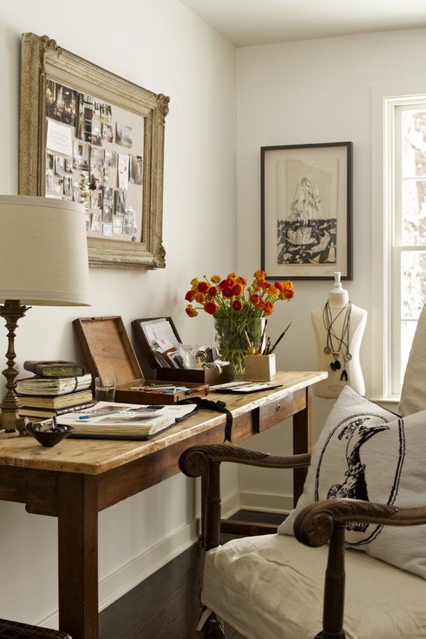 A vintage farmhouse home office with a wooden desk, a refined chair, chic artworks and a table lamp and blooms