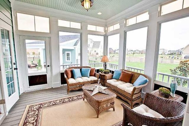 A farmhouse sunroom with rattan furniture, a rug, lamps and bright pillows that make the space more welcoming