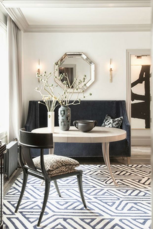 A black and white art deco inspired dining space with a black sofa, a catchy dining table, a chair, a geometric floor and a geometric mirror on the wall