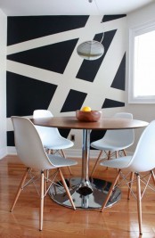 a modern black and white dining space with geometric decor on the wall, a round table and white chairs is a cool and bold nook