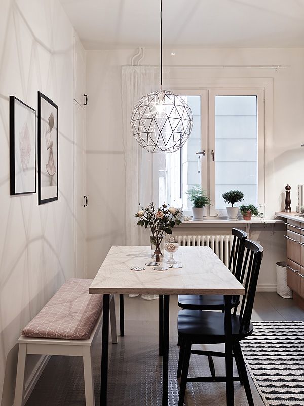 A Scandinavian dining space with a light stained table, black chairs, a bench with a geometric cushion and a geometric pendant lamp
