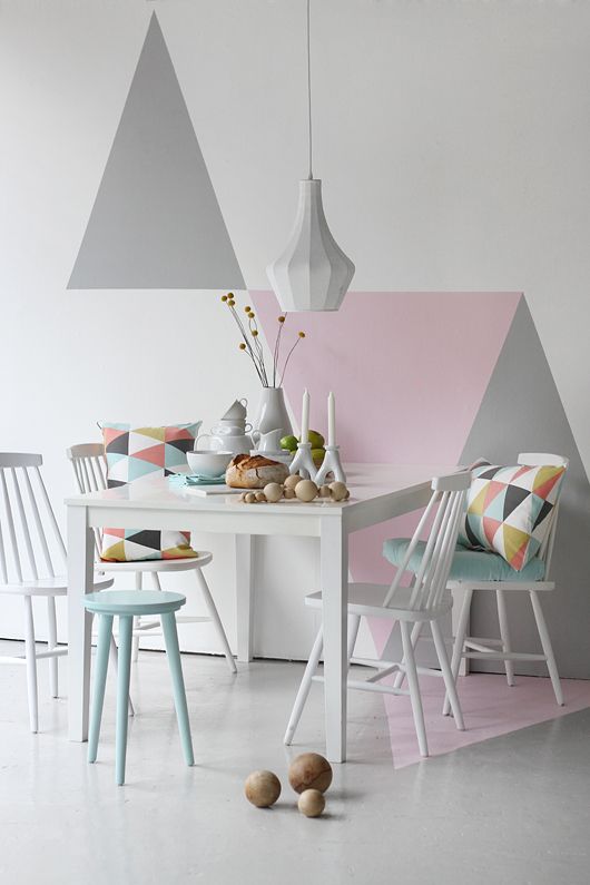 a beautiful pastel Scandinavian dining room with a white table, mint and white chairs and stools, geometric mural on the wall, geo pillows and a faceted pendant lamp