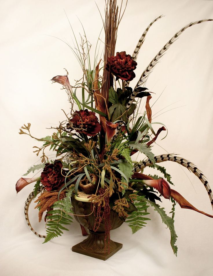 A stylish fall centerpiece of a vintage urn, greenery, feathers and faux blooms is an elegant boho inspired decoration to make for fall