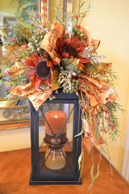 A fall candle lantern with a rust colored candle, dried grasses, berries and faux blooms and plaid ribbons for the fall