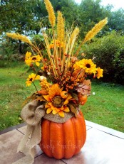 a fall arrangement of a faux pumpkins, a burlap bow, bright faux blooms, berries and branches is a stylish centerpiece