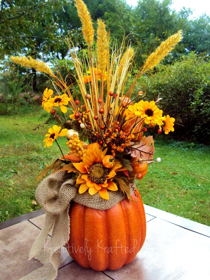 A fall arrangement of a faux pumpkins, a burlap bow, bright faux blooms, berries and branches is a stylish centerpiece