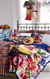a bright boho bedroom with a light blue dresser, a forged bed with bold floral bedding, colorful pendant lamps and crochet blankets