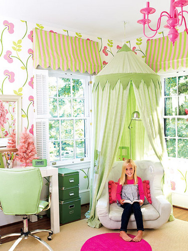 a colorful kid's room with bright floral wallpaper, a white desk, a light green chair, a dark green cabinet and a chair with a light green canopy over it