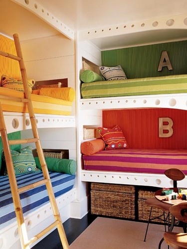 A colorful shared kid's room with a grene, red, yellow and blue built in bunk beds, a ladder and colorful and printed pillows