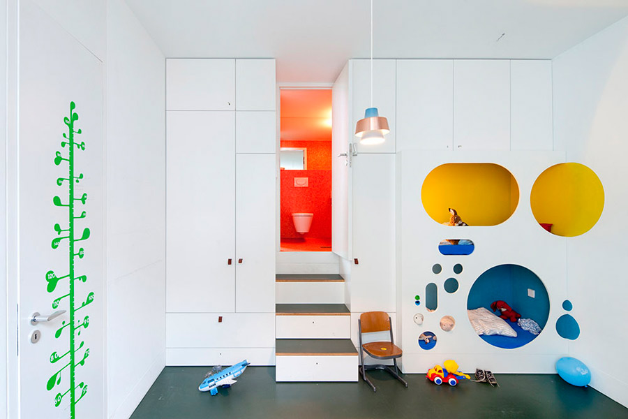 A white kid's room with a quirky design   a bed and a reading space hidden inside a white unit with colorful circles and sleek storage units around