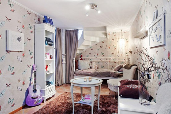 a beautiful and delicate kid's space with butterfly wallpaper, white furniture - a bed, a storage unit, comfy chairs and lilac and purple textiles