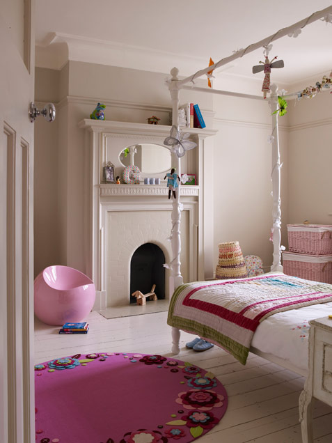 A greige girl's room with a non working fireplace, a canopy bed with neutral and fuchsia bedding, a hot pink rug and a sleek pink chair
