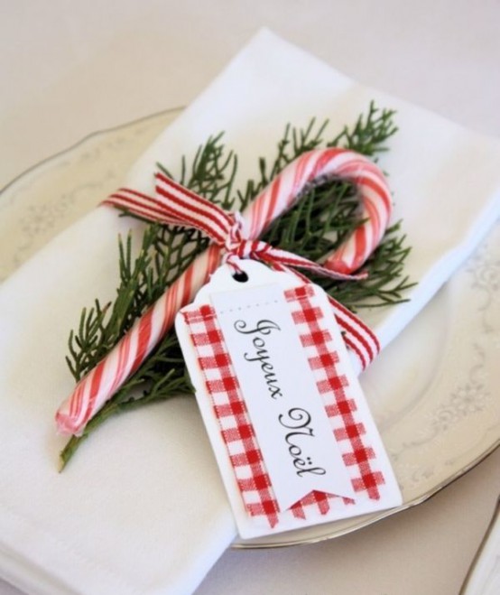 a Christmas place setting done with white porcelain, white linens, a fir twig, a candy cane and a tag is a fun and bold idea
