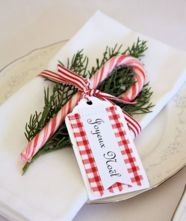 A Christmas place setting done with white porcelain, white linens, a fir twig, a candy cane and a tag is a fun and bold idea