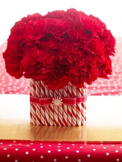 a bright Christmas centerpiece of a vase with red blooms and lots of candy canes covering it is a very chic and lovely idea