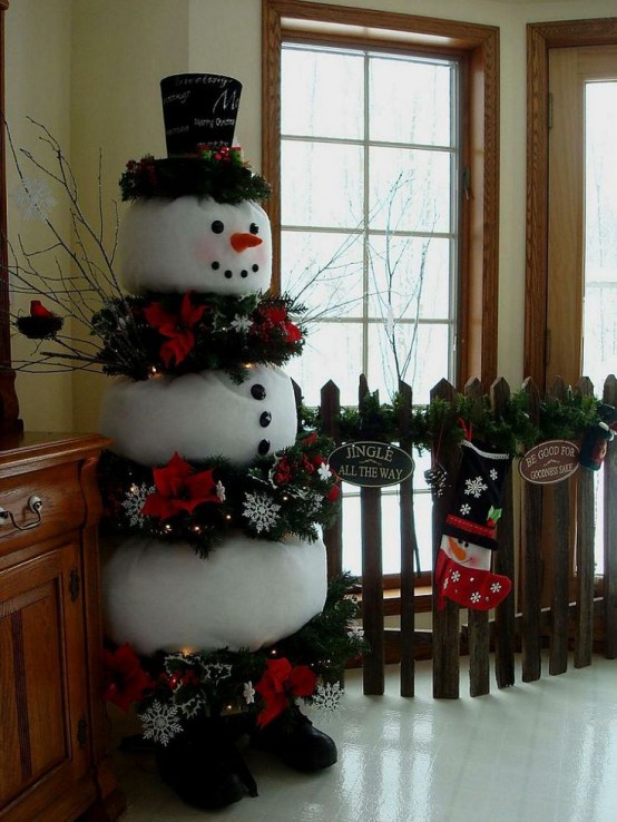 a alrge and bold snowman decoration  with evergreens, snowflakes and red blooms, twigs and a tall hat with words is a cool idea for outdoors and indoors