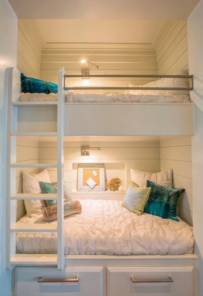 Cozy built in bunk beds in white with wall sconces over each bed and a single ladder to reach the upper sleeping space