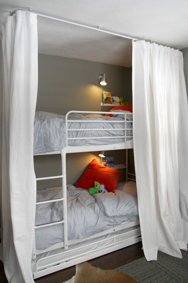 A white metal kids' bunk bed unit with a ladder attached and wall sconces plus curtains to keep the sleeping spaces private