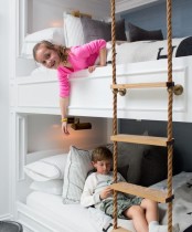 a kids’ bunk bed setup with wall sconces and a rope ladder to reach each sleeping space
