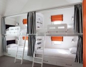 a functional kids’ bunk bed setup done in white, greys and with orange accents, with ladders and lights