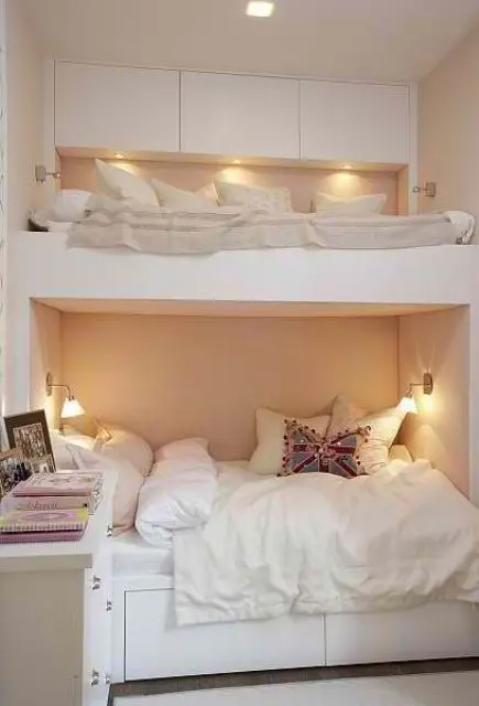 A minimalist white bunk bed unit with a sleek storage space with built in lights and wall sconces over the lower bed
