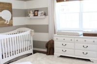 a neutral farmhouse nursery with a striped accent wall, white vintage furniture, a white faux fur rug, woven shades, neutral bedding
