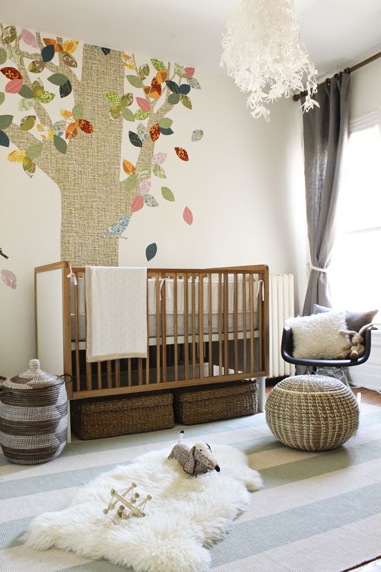 A gender neutral nursery with mid century modern and boho furniture, a tree on the wall and cozy and simple textiles including faux fur