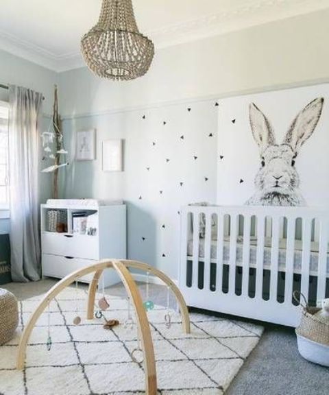 a gender neutral nursery with a printed wall, white modern furniture, a beaded chandelier and artworks and toys