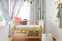 a stylish gender neutral nursery with simple and minimal furniture, grey curtains, colorful bedding and a bold mustard tassel garland
