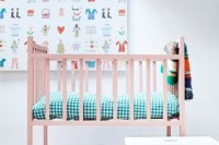 a gender neutral nursery with a pink bed, colorful bedding and textiles, a bold artwork and some accessories