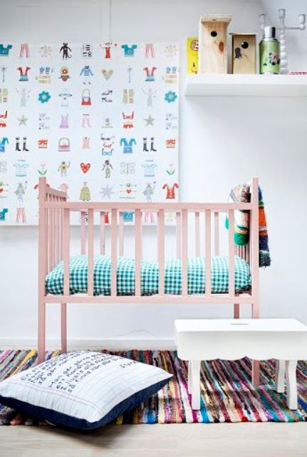 a gender neutral nursery with a pink bed, colorful bedding and textiles, a bold artwork and some accessories