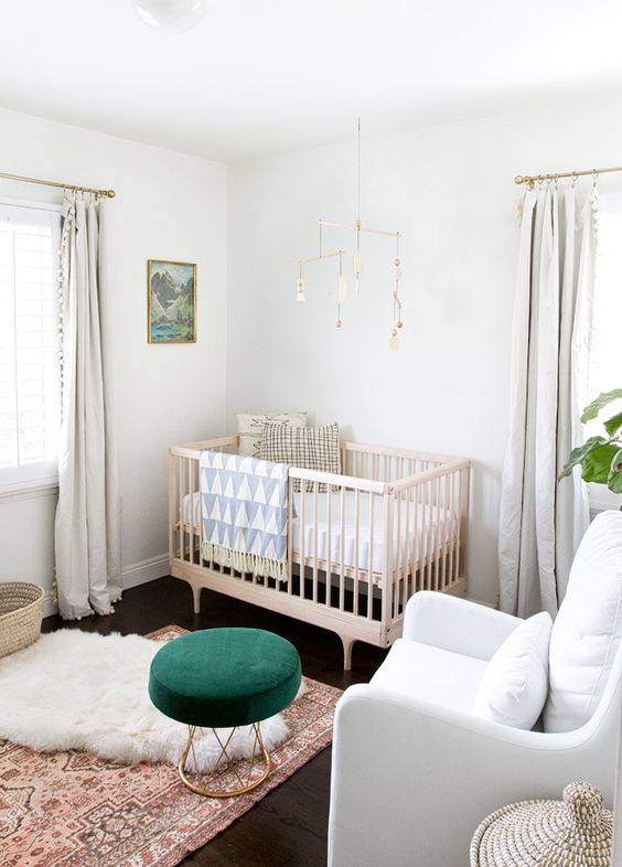 a gender neutral space with neutral textiles and upholstery, a wooden crib and a bright emerald ottoman and prints to enliven the space