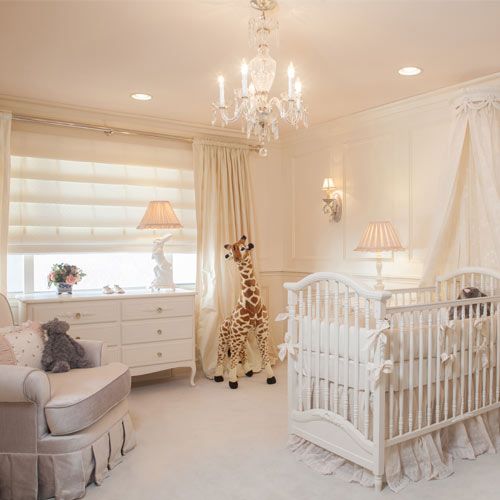 a gender-neutral and neutral nursery with vintage glam touches, a crib with ruffles, a glam vintage chandelier, curtains and shades and some pretty toys