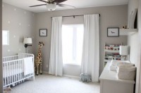 a gender neutral nursery done in grey and white, with elegant white furniture, a polka dot wall and open shelves with books