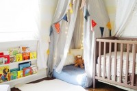 a colorful gender neutral nursery with a wooden crib, a teepee, colorful garlands and banners and bright books on the shelf