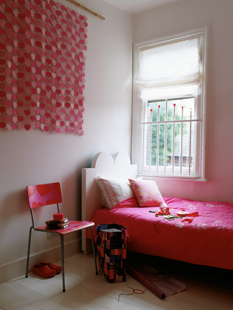 A contrasting girl's room with all neutral everything, hot pink bedding, a pink chair and a pink heart hanging and neutral pillows